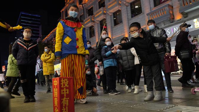 Seorang anak melemparkan tongkat ke dalam wadah untuk memenangkan hadiah di sepanjang shopping street di Wuhan, China, Jumat (15/1/2021). Selain masker, orang-orang menjalani kehidupan sehari-hari mereka seperti sebelumnya di Wuhan, tempat pertama kali virus corona terdeteksi. (AP Photo/Ng Han Guan)