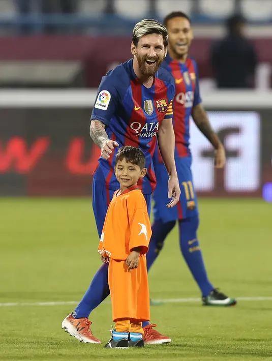 Bintang Barcelona Lionel Messi berbincang dengan bocah Afghanistan, Murtaza Ahmadi jelang laga melawan Al Ahli di Doha,  Selasa (13/12). Murtaza menjadi sensasi di internet karena mengenakan plastik bernomor punggung 10 untuk Messi. (Karim Jaafar/AFP)