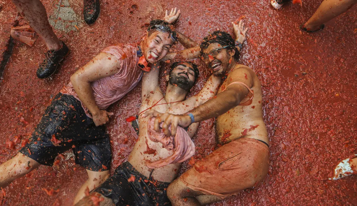 Orang-orang yang bersuka ria berbaring di genangan tomat yang tergencet selama "Tomatina" tahunan, pesta pertarungan tomat di desa Bunol dekat Valencia, Spanyol, Rabu (31/8/2022). Biasanya pertempuran berlangsung selama satu jam, setelah sebagian besar area di alun-alun kota penuh dengan tomat. (AP Photo/Alberto Saiz)