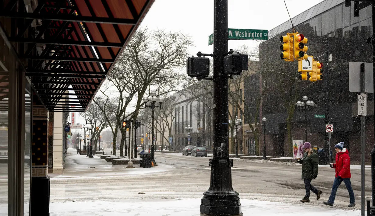 Dua wanita berjalan di Washington Street saat salju turun di Ann Arbor, Michigan, Rabu (2/2/2022). Badai salju membuat maskapai membatalkan ratusan penerbangan. (Jacob Hamilton/Ann Arbor News via AP)