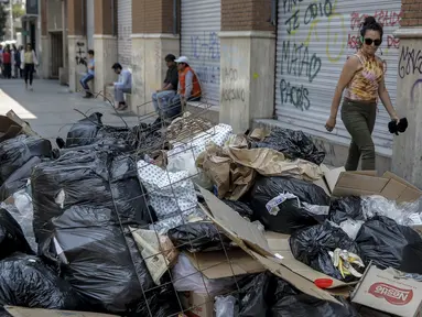 Seorang wanita berjalan melewati tumpukan sampah akibat pemogokan petugas sampah di Santiago (14/11/2019). Protes kekerasan meletus di ibukota Chile, Santiago, pada Selasa ketika mata uang negara itu turun ke level terendah dalam sejarah. (AFP/Javier Torres)