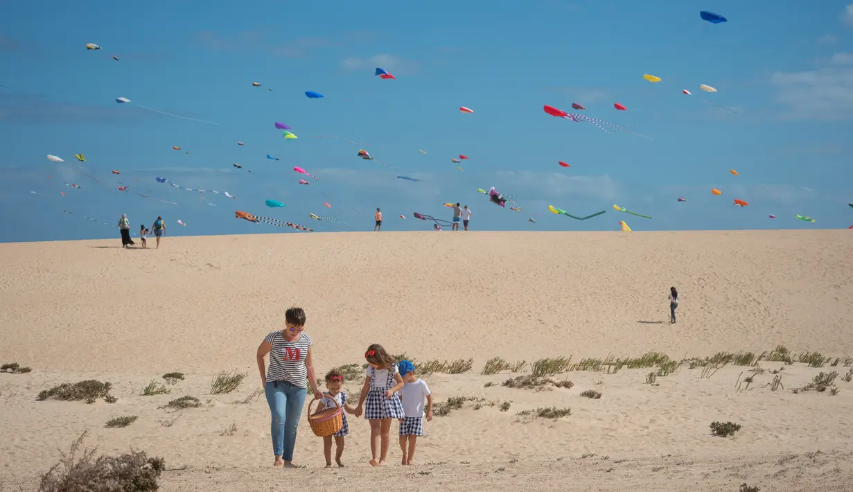 Sebuah keluarga melintas saat Festival Layang-layang Internasional di Fuerteventura, kepulauan Canary, Spanyol, 10 November 2018. Festival diikuti 45 penerbang layang-layang profesional dan amatir dari delapan negara. (DESIREE MARTIN/AFP)