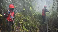 Petugas pemadam kebakaran menyemprotkan air untuk memadamkan kebakaran di Kampar, provinsi Riau pada 17 September 2019. Kebakaran hutan dan lahan (karhutla) yang masih terjadi membuat sejumlah wilayah di Provinsi Riau terpapar kabut asap. (ADEK BERRY / AFP)