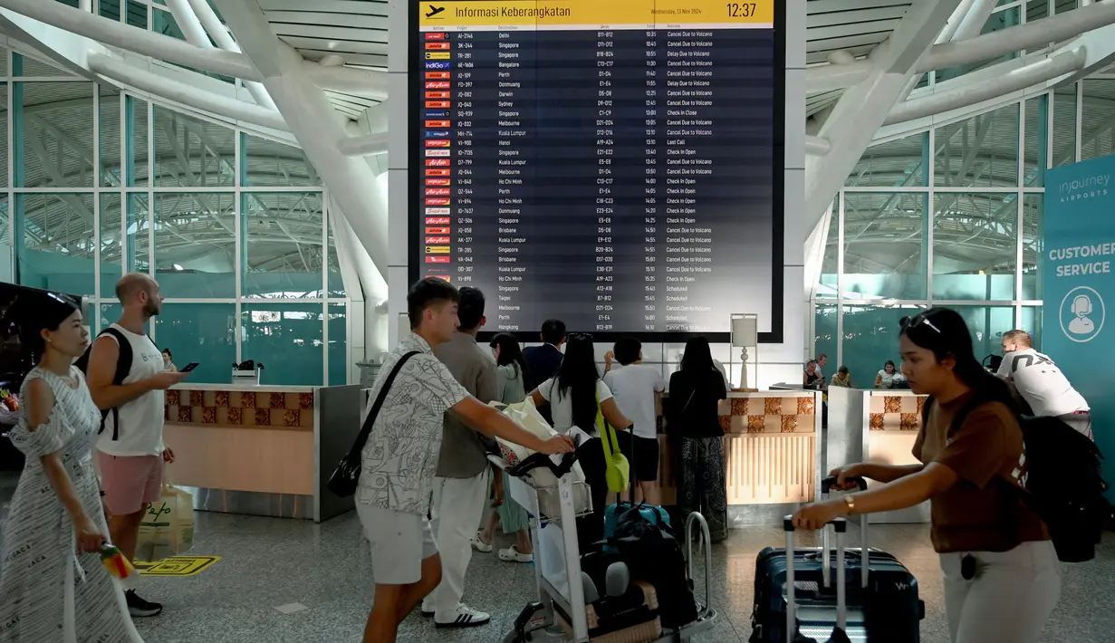 Para penumpang melihat papan elektronik yang menampilkan penerbangan yang dibatalkan di Bandara Internasional Ngurah Rai, Denpasar, Bali, Rabu 13 November 2024. (SONNY TUMBELAKA/AFP)