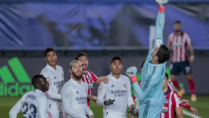 Kiper Real Madrid, Thibaut Courtois menepis bola saat bertanding melawan Atletico Madrid pada pertandingan La Liga Spanyol di stadion Alfredo Di Stefano, Spanyol, Minggu (13/12/2020). Madrid menang atas Atletico 2-0. (AP Photo/Bernat Armangue)