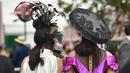 Dua orang wanita berjalan memakai hiasan kepala saat menyaksikan kompetisi balap kuda Melbourne di arena pacuan kuda Flemington Racecourse di Melbourne, Australia (1/11). Balap kuda ini diselenggarakan pertama kalinya pada tahun 1861. (AFP/Paul Crock)