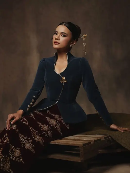 Sementara itu, Audi Marissa memilih gaya yang lebih klasik dan artsy. Ia tampil mengenakan kebaya kutu baru modern berwarna navy dengan detail trim emas yang memberi kesan sophisticated. Potongan peplum di bagian pinggang membuat siluet tubuhnya terlihat anggun, sementara kain batik warna maroon dengan motif emas memberi sentuhan tradisional yang kaya. Rambut sleek bun dengan aksesori emas di sisi kepala semakin menyempurnakan penampilannya yang terlihat seperti perempuan bangsawan Jawa modern. [@audimarissa],