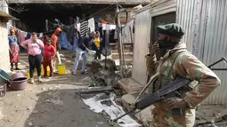 Orang-orang berdiri dekat rumah mereka dan menyaksikan anggota Pasukan Pertahanan Afrika Selatan (SANDF) berpatroli di daerah mereka di Alexandra, Johannesburg, Kamis (15/7/2021). Patroli tersebut menyusul kerusuhan massa yang disebabkan dipenjaranya mantan Presiden Jacob Zuma. (Phill Magakoe/AFP)