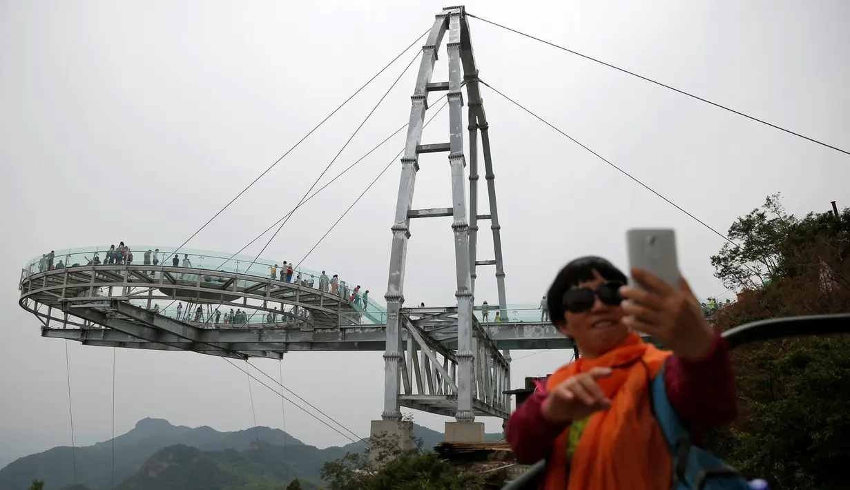 Seorang wanita berfoto selfie dengan latar belakang platform kaca di Jurang Shilin, Beijing, Cina, (27/5). Wahana ini hanya ditujukan bagi mereka yang bernyali. (REUTERS/Kim Kyung-Hoon)