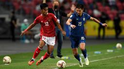 Pemain Indonesia Pratama Arhan Alif Rifai (kiri) berebut bola dengan pemain Thailand Narubadin Weerawatnodom pada pertandingan sepak bola leg kedua final Piala AFF 2020 di National Stadium, Singapura, Sabtu (1/1/2022). Pertandingan berakhir dengan skor 2-2. (Roslan RAHMAN/AFP)