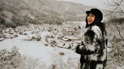 Liburan ke Jepang, gadis berusia 26 tahun ini menggunakan busana hangat serba hitam lengkap dengan topi hitam. Pemandangan perumahan berbalut salju di Shirakawa Go menjadi latar fotonya, menambah keindahan. (Liputan6.com/IG/@jscmila)