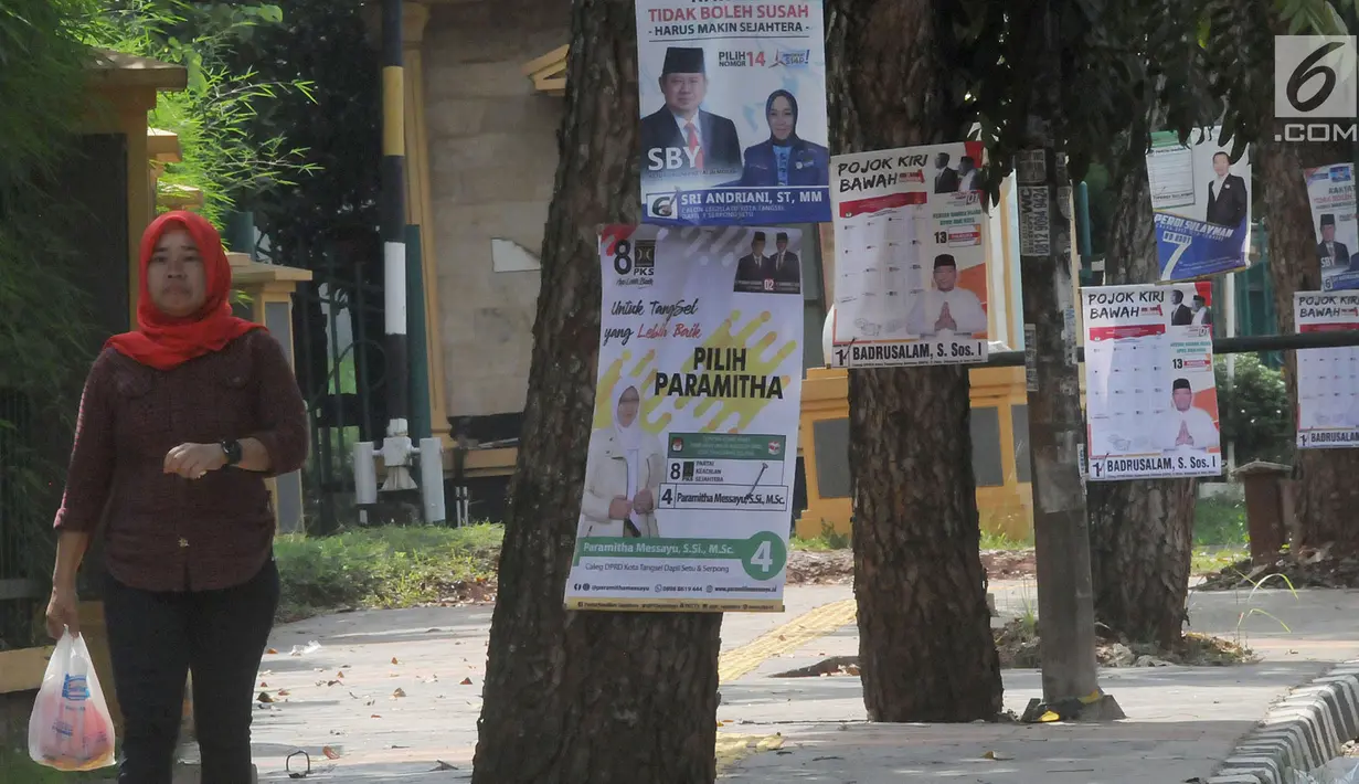 Pejalan kaki melintas dekat Alat Peraga Kampanye (APK) yang dipasang di pohon kawasan Ciater, Tangerang selatan, Senin (1/4). Pemasangan APK sejumlah caleg yang dipaku di pohon melanggar peratuan KPU Nomor 15 Tahun 2013 tentang tata cara pemasangan APK pemilihan umum. (merdeka.com/Arie Basuki)