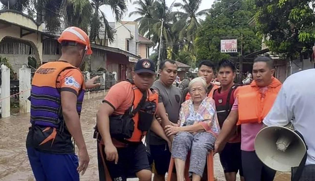 Seorang wanita tua duduk di kursi sambil digendong oleh personel penjaga pantai yang mengarungi banjir di Plaridel, provinsi Misamis Occidental di Filipina selatan, Senin, 26 Desember 2022. Hujan lebat dan banjir menghancurkan beberapa bagian Filipina. (Philippine Coast Guard via AP)