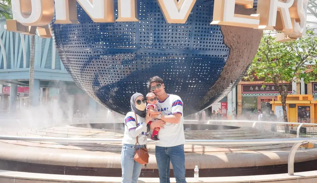 Rizky Billar dan Lesti Kejora memilih Singapura untuk liburannya, tak berbeda dengan yang lain, mereka juga membawa Baby L. Mereka pun berpose di bola dunia Universal yang menjadi ciri khas para turis.  (Foto: Instagram/@rizkybillar)