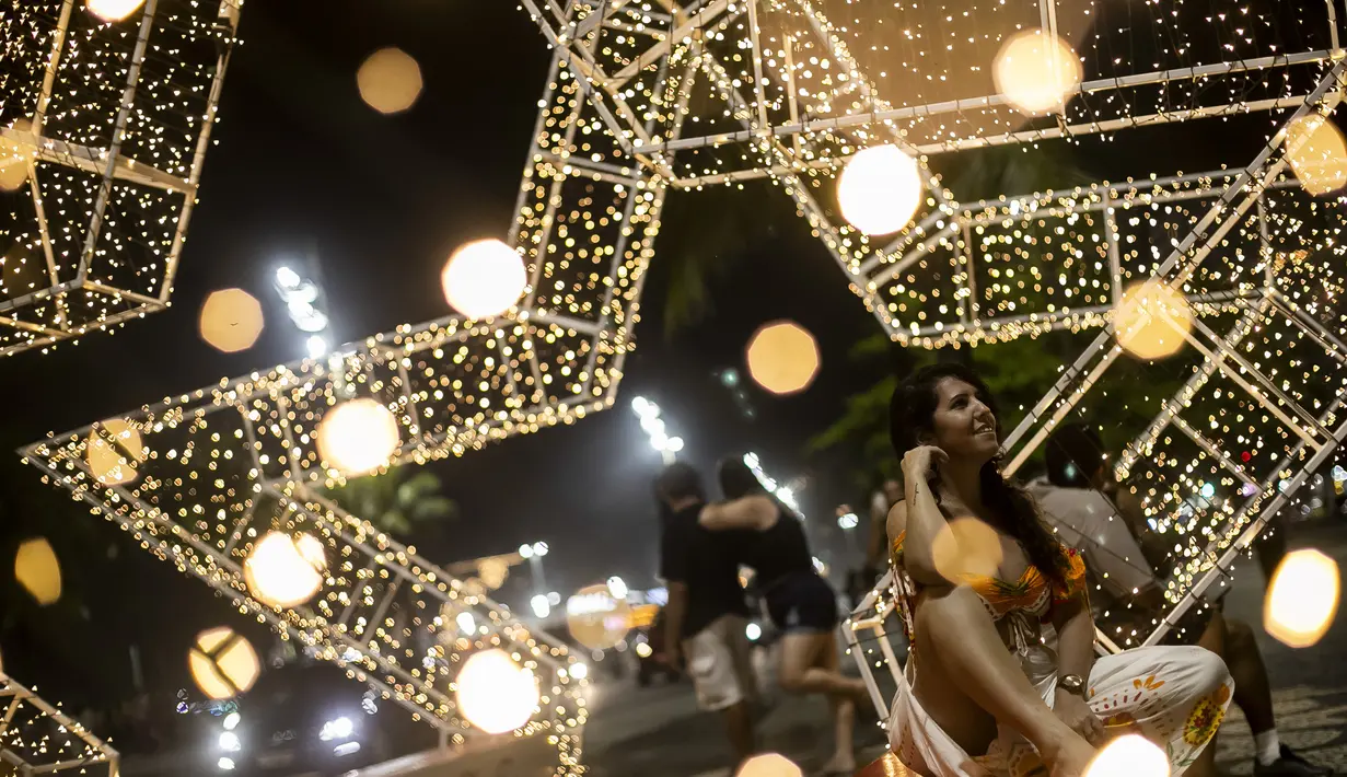 Seorang wanita duduk di sepanjang pantai Copacabana, dengan latar belakang lampu Natal di Rio de Janeiro, Brasil (11/12/2021). Jelang perayaan Natal, taman dan pantai dihiasi lampu-lampu yang indah. (AP Photo/Bruna Prado)