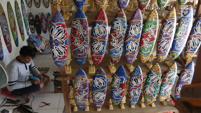 Pengrajin membuat sovenir papan seluncur di Bali, Senin (15/10). Menteri Koordinator Bidang Perekonomian Darmin Nasution meminta pelaku usaha sektor pariwisata dapat memanfaatkan KUR dengan bunga 7%. (Liputan6.com/Angga Yuniar)