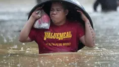 Seorang warga menggunakan bak cucian untuk melindunginya dari hujan saat ia menyeberangi jalan yang banjir akibat Badai Tropis Yagi, yang secara lokal disebut Enteng, di Cainta, provinsi Rizal, Filipina, Senin (2/9/2024). (AP Photo/Aaron Favila)