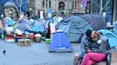 Pasangan tunawisma memainkan ponsel di depan perkampungan tenda para tunawisma di kawasan Martin Place, pusat kota Sydney, Rabu (9/8). Sydney kini tak hanya dipenuhi gedung bertingkat, tetapi juga disesaki tenda-tenda tunawisma. (PETER PARKS / AFP)