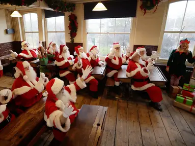Sejumlah pria mengenakan kostum Santa Claus terlihat beradegan sedang belajar saat sesi pemotretan di Ragged School Museum di London (16/11). Mereka melakukan sesi pemotretan untuk Ministry of Fun Santa School. (AP Photo/Matt Dunham)