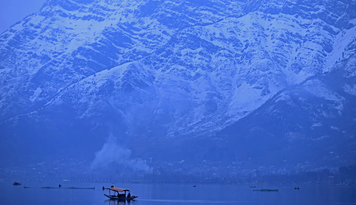 Orang-orang menikmati perjalanan dengan perahu dengan latar belakang pegunungan yang tertutup salju di danau Dal di Srinagar (11/1/2022). Danau Dal yang merupakan danau terbesar kedua di propinsi Jammu dan Kashmir negara bagian India ini merupakan pusat pariwisata dan rekreasi. (AFP/Tauseef Mustafa)