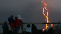 Warga melihat guguran lava pijar yang keluar dari gunung api Piton de la Fournaise atau Peak of the Furnace di Pulau Reunion, Samudera Hindia, Prancis, Selasa (13/8/2019). Letusan Piton de la Fournaise berlanjut hingga hari ketiga. (Richard BOUHET/AFP)