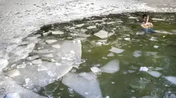 Seorang pria mandi di lubang es di danau dekat Vilnius, Lithuania, Minggu (13/2/2022). Suhu udara 0 derajat Celcius (32 derajat Fahrenheit). (AP Photo/Mindaugas Kulbis)