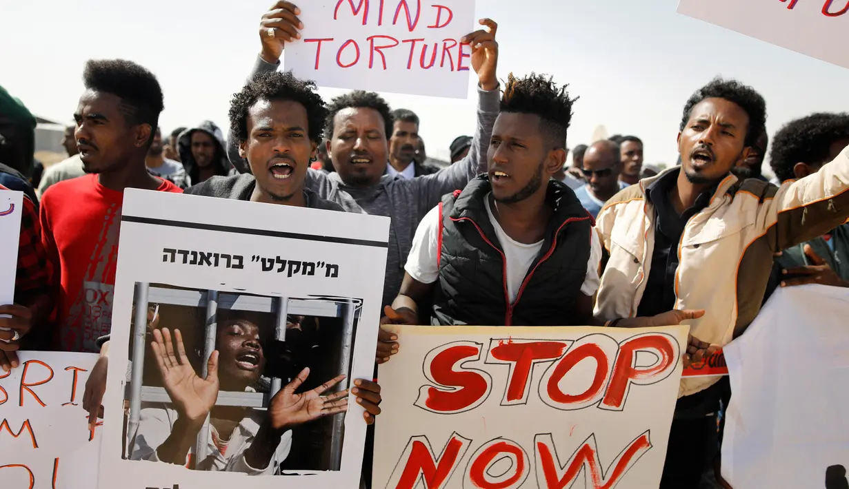 Migran Afrika membawa poster dan foto rekan mereka yang ditahan pemerintah Israel saat melakukan aksi di Penjara Saharonim, Israel (22/2). Sebelumnya, Israel mengusir puluhan ribu imigran Afrika. (AFP Photo/Menahem Kahana)
