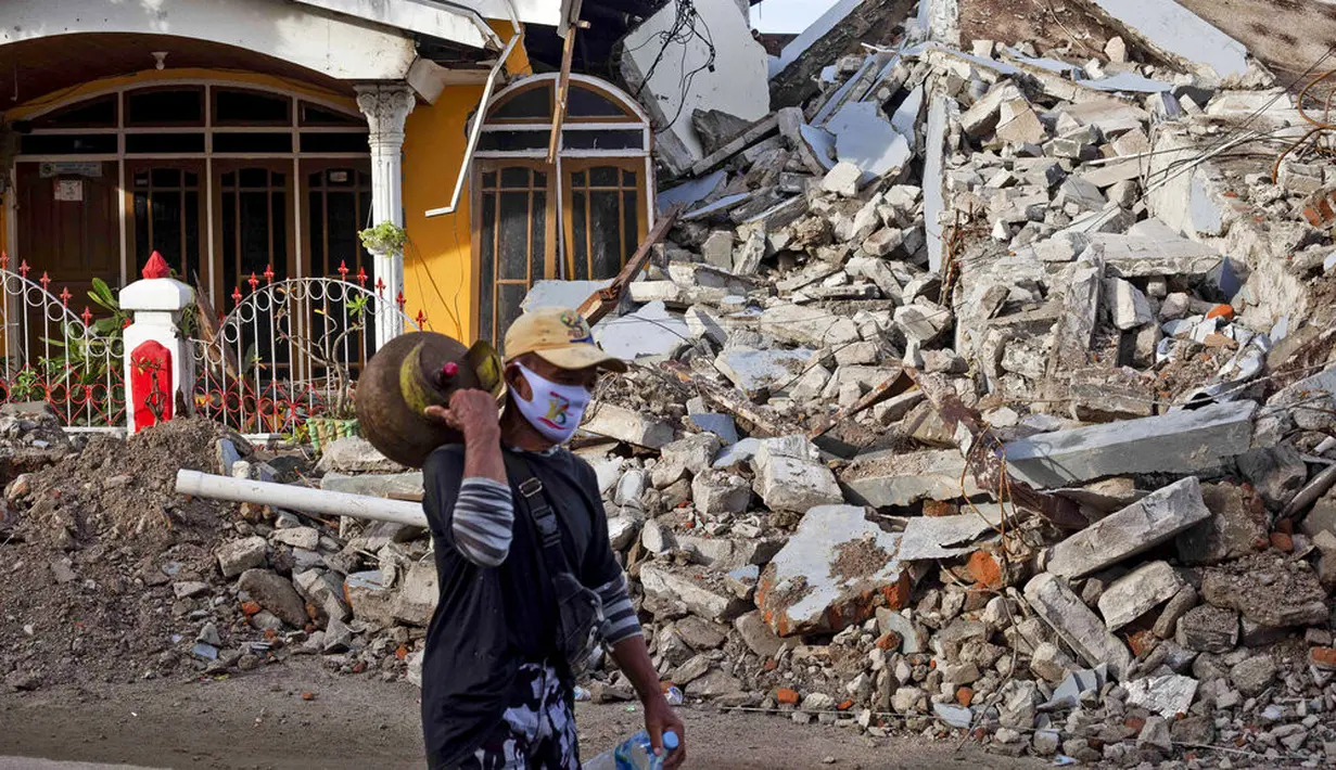 Seorang pria berjalan melewati rumah yang ambruk akibat gempa di Mamuju, Sulawesi Barat, Indonesia, Senin (18/1/2021). BNPB menyatakan pelabuhan hingga rumah sakit di Kabupaten Mamuju rusak berat akibat guncangan gempa dengan magnitudo 6,2. (AP Photo/Yusuf Wahil)