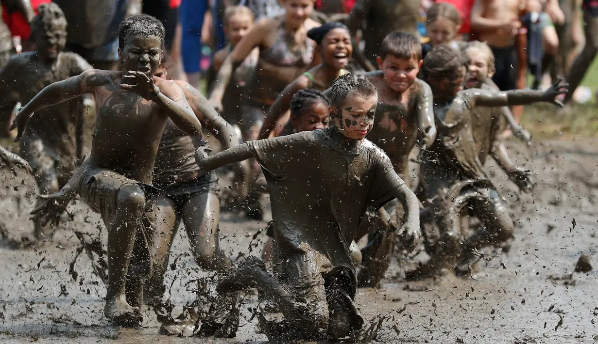 Anak-anak berlari ke dalam kubangan berisi lumpur saat Mud Day atau Hari Lumpur di Michigan, negara bagian AS, Selasa (9/7/2019). Para peserta perayaan yang menjadi tradisi setiap tahun ini merupakan anak-anak untuk agar mereka bersenang-senang selama liburan musim panas.  (AP/Carlos Osorio)