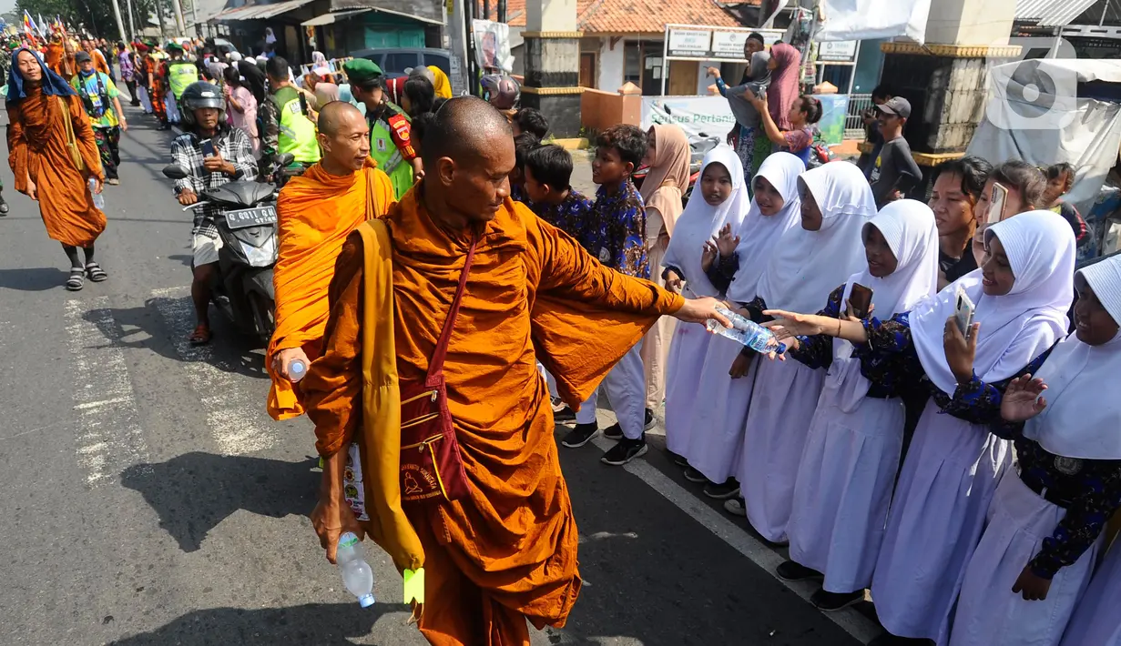 Para murid sekolah dasar berdiri di pinggir jalan raya sambil menyemati para Biksu. Selain murid SD, para Biksu juga disamut warga setempat dan umat dari agama lain. (merdeka.com/Arie Basuki)