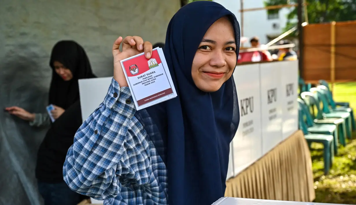 PIlkada Serentak 2024 Sukses Dilaksanakan. Seorang perempuan menunjukkan kertas suara saat pemilihan kepala daerah untuk memilih gubernur, walikota dan bupati di Darul Imarah, pinggiran Banda Aceh, pada 27 November 2024. (CHAIDEER MAHYUDDIN/AFP)