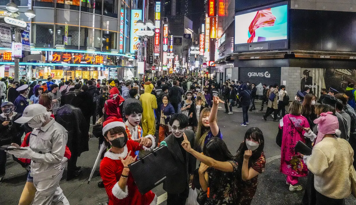 Para pejalan kaki dengan kostum berpose untuk foto ketika ribuan orang berkumpul di distrik Shibuya, area pertemuan populer untuk Halloween, di Tokyo, Minggu (31/10/2021). Daerah di sekitar Stasiun Shibuya dipadati anak-anak muda yang berdandan selama Halloween setiap tahun. (AP Photo/Kiichiro Sato)