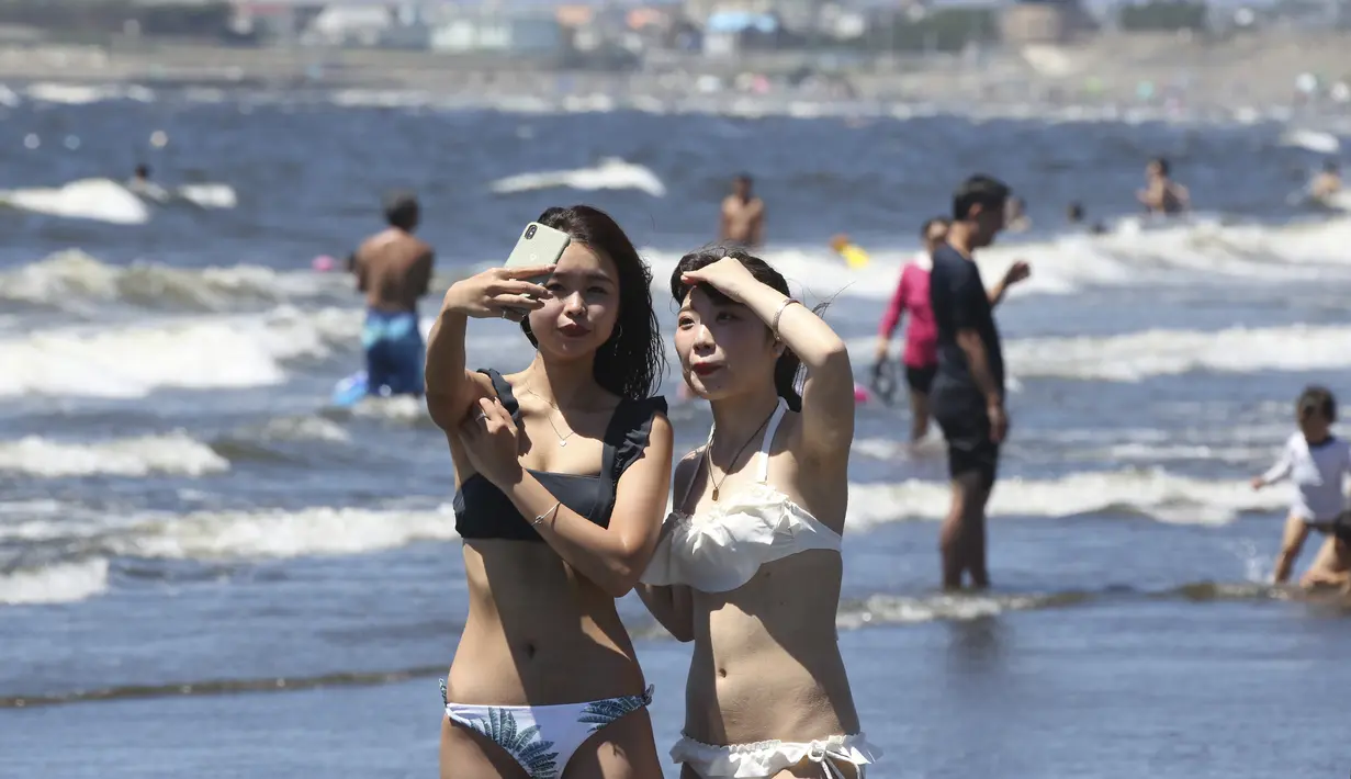 Dua wanita berselfie selama teriknya musim panas di Pantai Shonan di Fujisawa, dekat Tokyo, Selasa, (11/8/2020). (AP / Koji Sasahara)