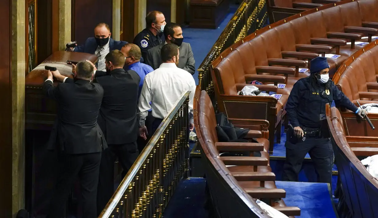 Polisi berdiri dekat pintu sambil menodongkan pistol saat pengunjuk rasa mencoba masuk ke Gedung Capitol Hill di Washington DC, Amerika Serikat, Rabu (6/1/2021). Beberapa di antara pengunjuk rasa nekat menerobos dan berusaha memasuki gedung. (AP Photo/Andrew Harnik)