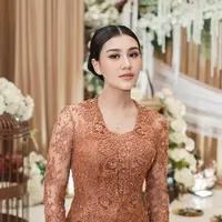 Tampil dalam balutan kebaya brokat cokelat, ia memancarkan aura keibuan yang tenang dengan sentuhan makeup bernuansa peach yang lembut dan elegan. [@aaliyah.massaid].