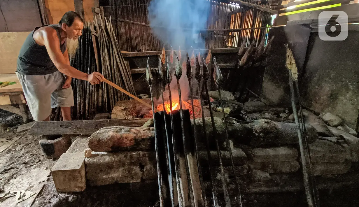 Uda Yunus mengasap ikan mas menggunakan kayu bakar di Setu Tujuh Muara Sawangan, Depok, Minggu (19/06/2022). Uda Yunus atau Muhammad Yunus telah menekuni metode ikan asap dan membuka warung makan di  pinggir Setu Tujuh Muara sejak 23 tahun yang lalu. (Liputan6.com/Fery Pradolo)