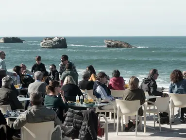 Warga dan turis menikmati minuman di sebuah kafe selama cuaca musim dingin yang hangat di sepanjang garis pantai kota Biarritz di Perancis barat (17/2). Kota ini terletak di region Aquitane, Departemen Pyrénées-Atlantiques. (AFP Photo/Iroz Gaizka)