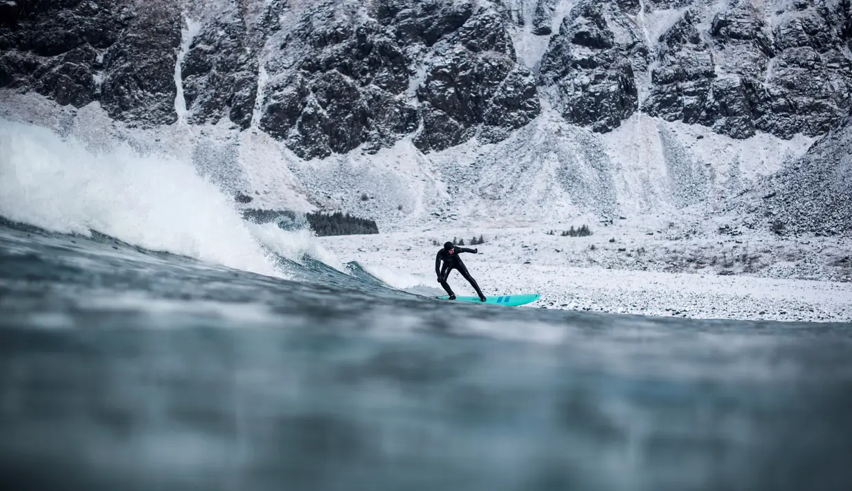 Seorang surfer menaiki papanya berselancar di melewati ombak di Unstad, Norwegia Utara (10/3). Peselancar ini menaklukan ombak dengan konidisi suhu minus 13 derajat Celsius. (AFP Photo/Olivier Morin)
