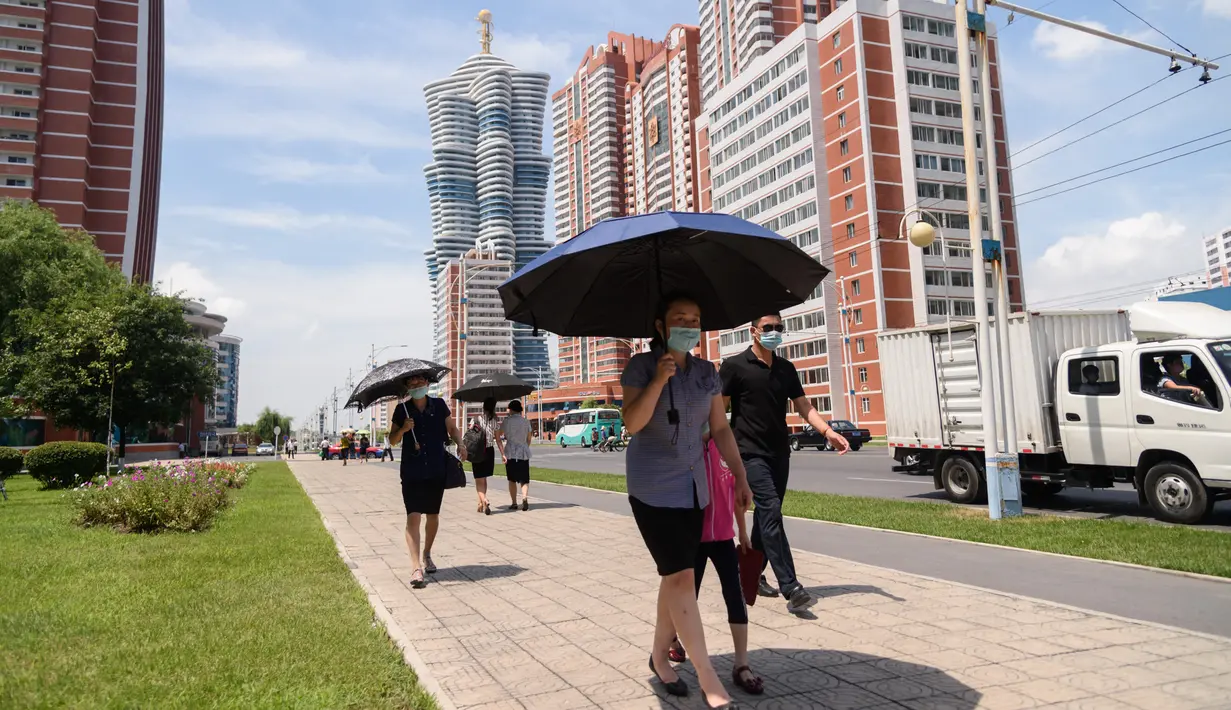 Orang-orang berlindung di bawah payung saat mereka berjalan di sepanjang Mirae Street selama suhu 34 derajat celsius, di Pyongyang, Korea Utara, Rabu (21/7/2021). Musim Panas dimulai pada bulan Juni hingga Agustus, dan puncak musim panas adalah bulan Agustus. (KIM Won Jin / AFP)