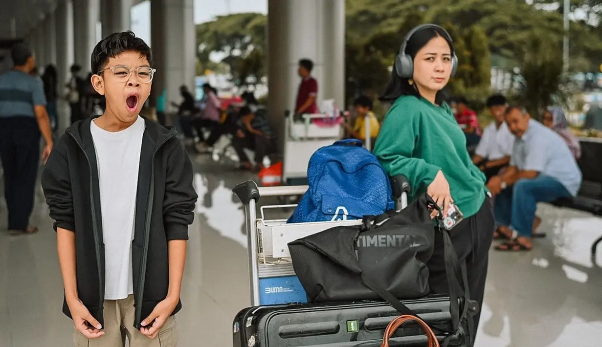 Gaya kasual kece Astrid Basjar dengan sweater hijau dan headphone di telinganya saat berangkat mudik. [@astridbasjar]