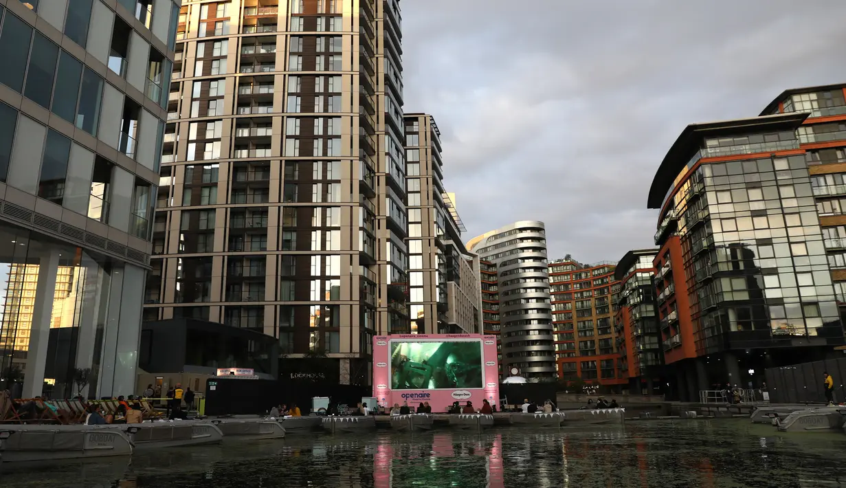Orang-orang duduk menonton film pada layar lebar saat acara pratinjau bioskop apung di Merchant Square di Kanal Regent, London, Rabu (1/9/2020). Bioskop bernama Openaireini itu memberi dua pilihan tempat duduk kepada penonton, yakni duduk di perahu atau di kursi di tepi kanal. (ISABEL INFANTES/AFP)