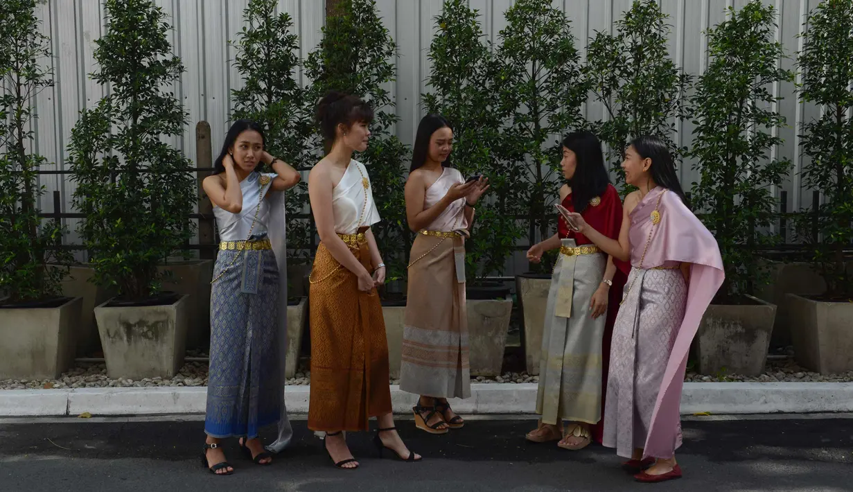 Para pekerja wanita mengenakan kostum tradisional berjalan bersiap mengikuti upacara keagamaan Buddha sebagai persiapan untuk festival tahun baru Songkran di luar kantor di Bangkok, Thailand (9/4). (AFP Photo/Romeo Gacad)