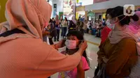 Seorang anak dipakaikan masker saat berada di Stasiun Gambir, Jakarta Pusat, Jumat (31/01). Dalam rangka pencegahan Virus Corona, PT Kereta Api Indonesia (persero) melakukan sosialisasi kepada penumpang kereta api dengan membagi-bagikan masker di stasiun Gambir. (merdeka.com/Imam Buhori)