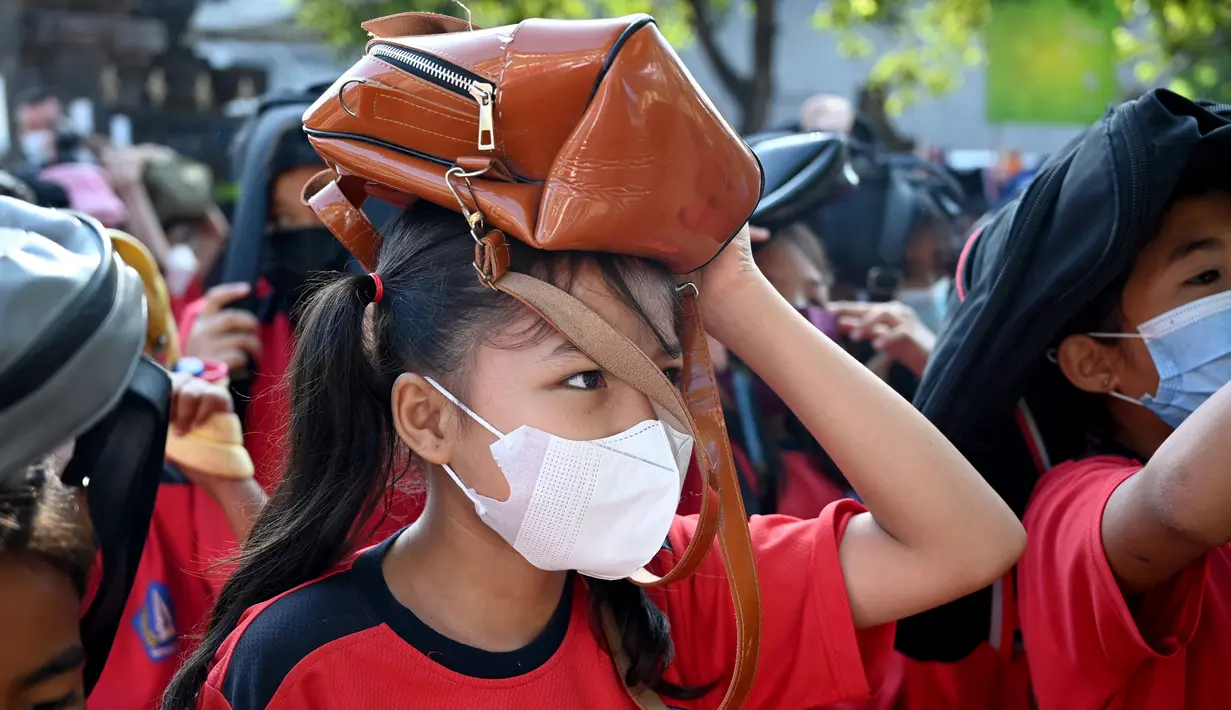 Anak-anak sekolah menggunakan tas mereka untuk melindungi diri saat latihan gempa dan tsunami di Tanjung Benoa, Kabupaten Badung, Bali, 24 Mei 2022. (SONY TUMBELAKA/AFP)