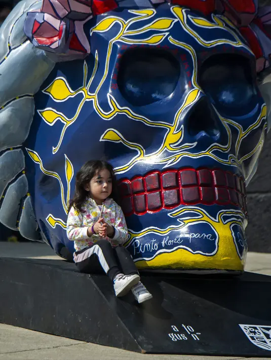 Seorang gadis berpose pada pameran Fridacraneos, tengkorak raksasa yang dilukis untuk menghormati mendiang seniman Meksiko Frida Kahlo, sebagai bagian dari perayaan Hari Kematian di Monumen Revolusi, Mexico City, Meksiko, 29 Oktober 2021. (Claudio CRUZ/AFP)