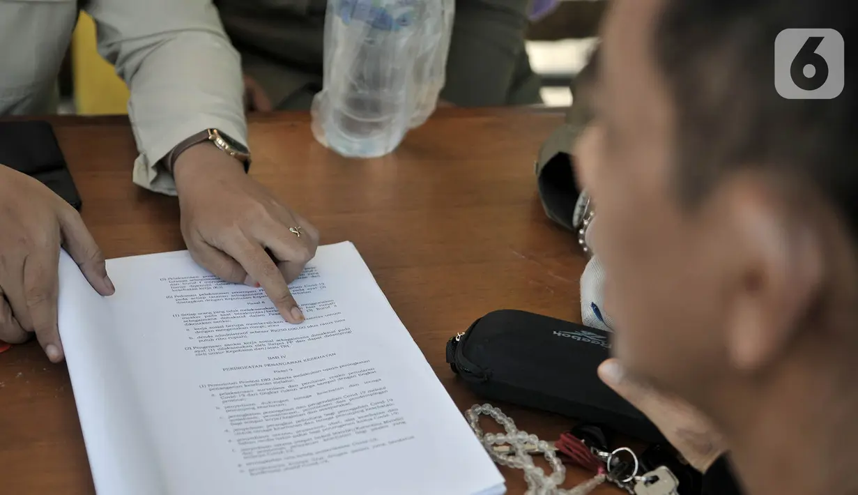 Petugas menunjukkan sanksi hukuman pelanggar PSBB yang tertuang dalam undang-undang di area Pasar Kramat Jati, Jakarta, Rabu (17/6/2020). (merdeka.com/Iqbal S. Nugroho)
