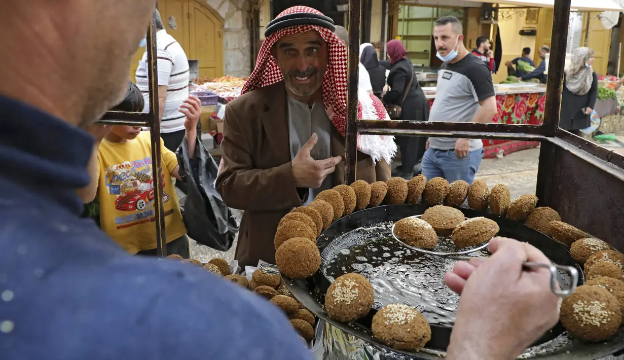 Seorang pria Palestina menunggu sejumlah falafel di sebuah penjual di kota Hebron di Tepi Barat yang diduduki, selama bulan suci Ramadhan, Minggu (18/4/2021). Falafel adalah sebuah makanan Timur Tengah yang pada bulan Ramadhan, sering dimakan sebagai hidangan buka puasa. (HAZEM BADER/AFP)