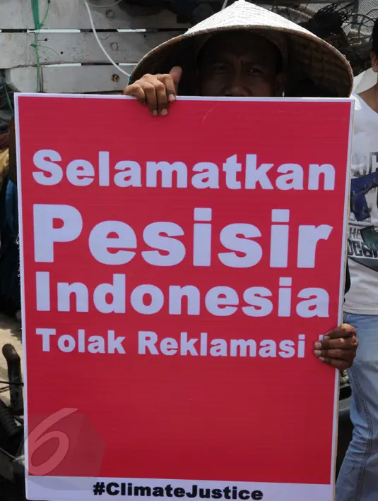 Seorang nelayan menunjukkan poster berisi penolakan terhadap proyek reklamasi Teluk Jakarta saat upacara sedekah bumi yang lebih dikenal dengan sebutan Nadran di Muara Angke, Jakarta, Minggu (13/12/2015). (Liputan6.com/Helmi Afandi)