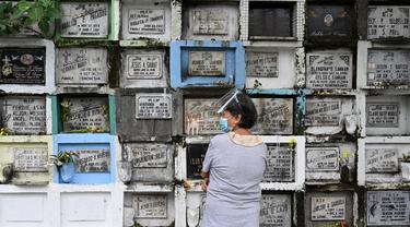Seorang wanita berdoa di depan makam seorang kerabat di sebuah pemakaman di Manila, Filipina (28/10/2021). Pemerintah setempat akan menutup pemakaman nasional untuk Hari Semua Orang Kudus karena pandemi virus corona Covid-19. (AFP/Ted Aljibe)