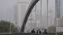 Orang-orang yang memakai masker untuk membantu mengekang penyebaran virus corona berjalan di atas jembatan di atas gedung perkantoran yang diselimuti kabut polusi di Beijing, Kamis (18/11/2021).  (AP Photo/Andy Wong)